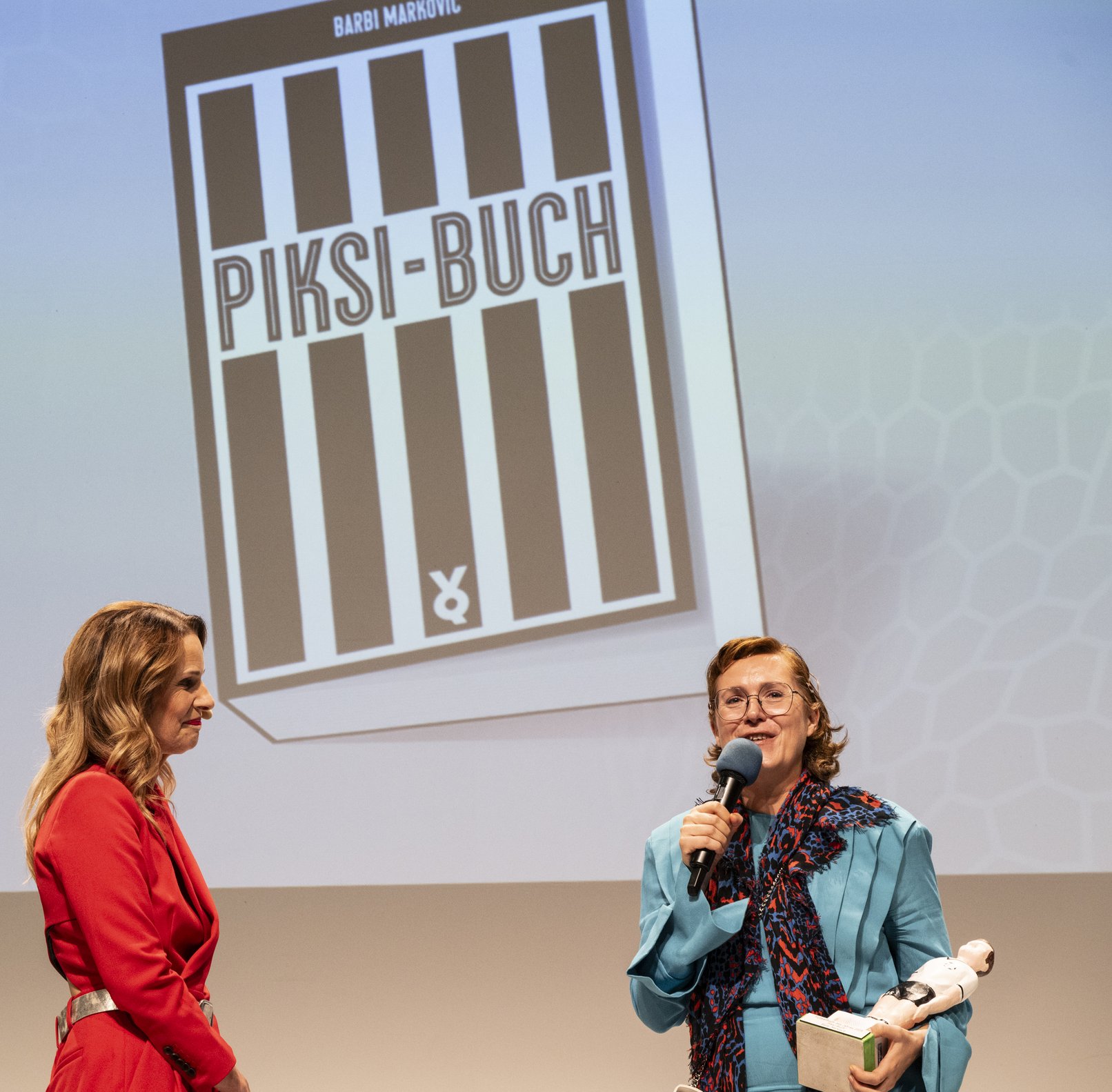 Kathrin-Müller-Hohenstein und Barbi Markovic, Autorin des Fußballbuchs des Jahres 2025 auf der Bühne beim Interview. Im Hintergrund der ein großes Foto vom Cover des Sieger-Buchs: Piksi-Buch.