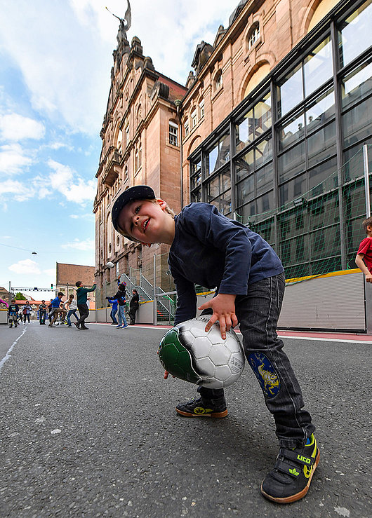 Ein Junge steht mit einem der dreieckigen Bälle auf dem Soccer-Court. Im Hintergrund spielen weitere Kinder mit den Bällen.