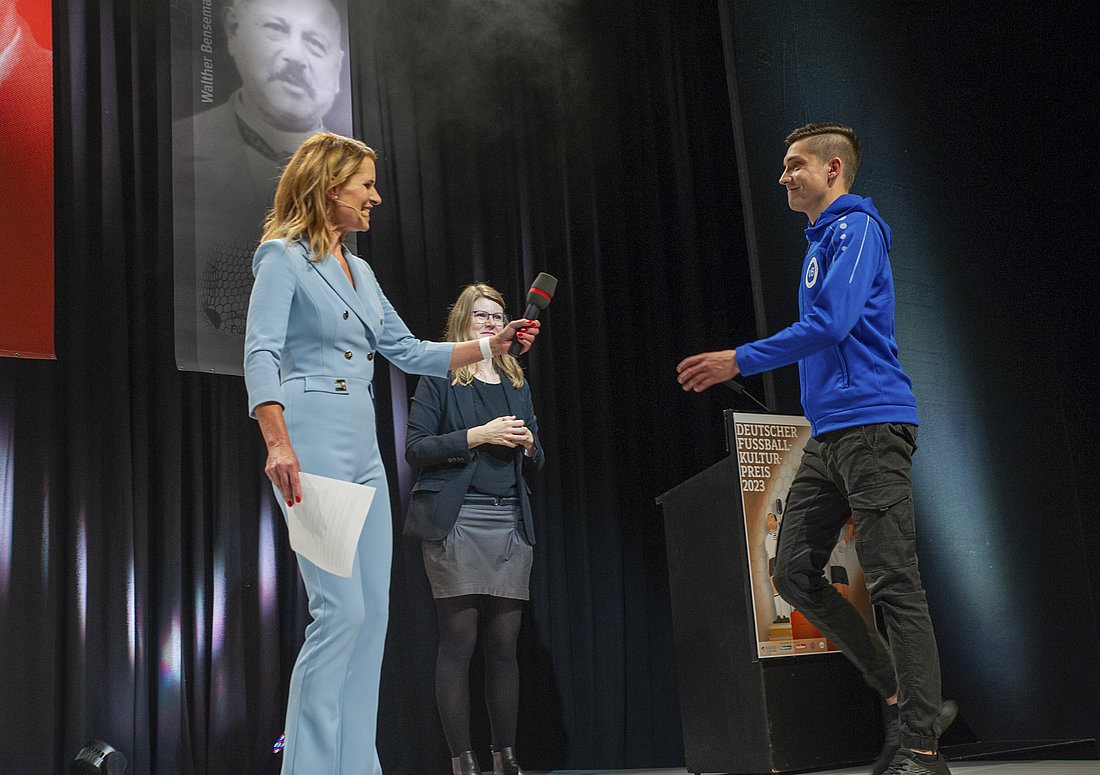 Moderatorin Katrin Müller-Hohenstein begrüßt den für den "Fußballspruch des Jahres" nominierten Sebastian Zeitler auf der Bühne und reicht ihm ein Mikrofon.